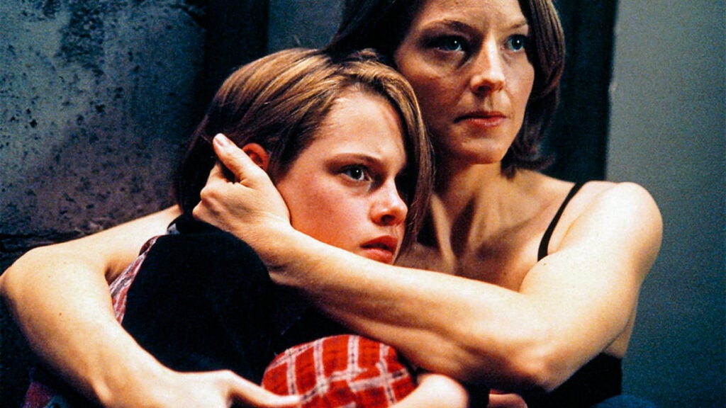 A woman in a black top protectively holds a young person in a red plaid shirt in a dimly lit room.