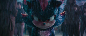 A fierce humanoid creature with blue and pink fur stands in the rain, glaring intently.