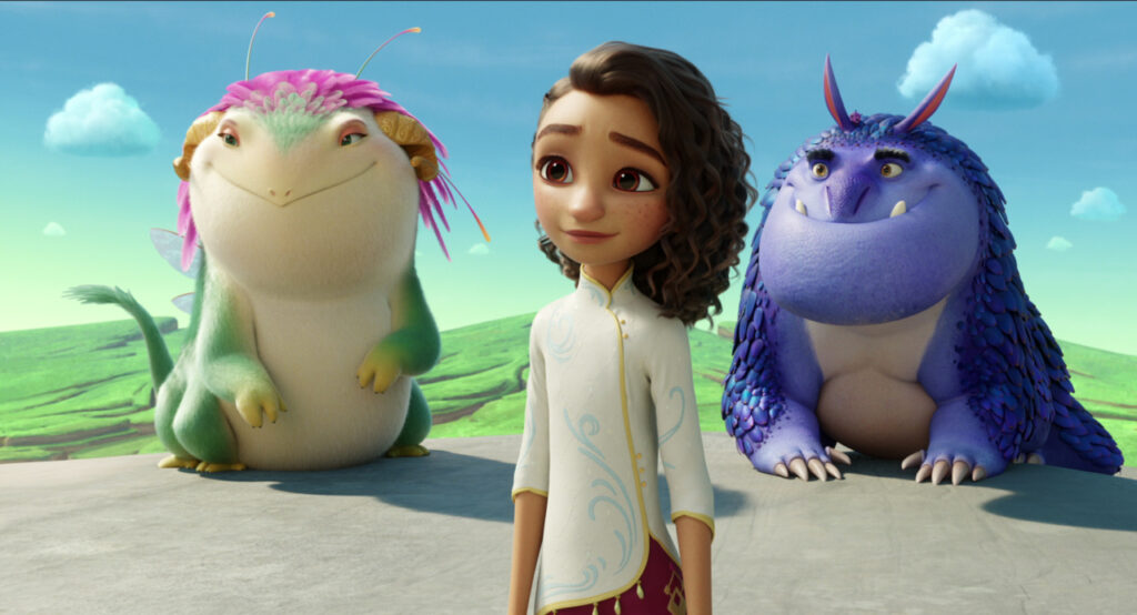 A young girl stands in front of two colorful creatures on a platform with a grassy landscape in the background.