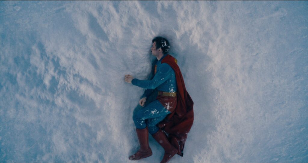 Person in a superhero costume lying on snowy ground, covered in snow.