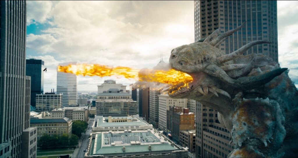 A large dragon breathes fire over a cityscape, with tall buildings and a clear sky in the background.