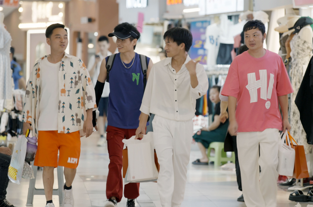 Four people walk through a shopping center, carrying shopping bags.