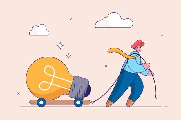 A person is dragging a large light bulb on a cart with clouds in the background.