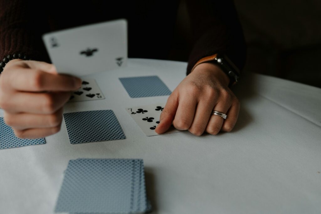 A person playing cards at a table, holding an ace of clubs, with other cards laid out.