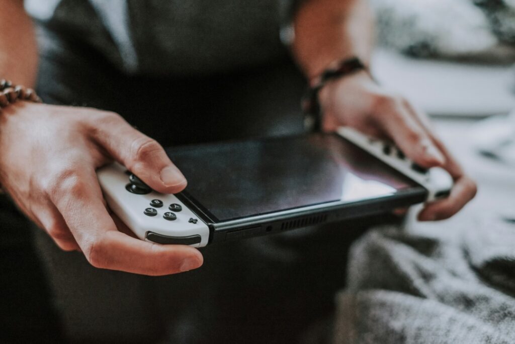 Person holding a portable gaming console with white controllers, resting on a gray fabric surface.