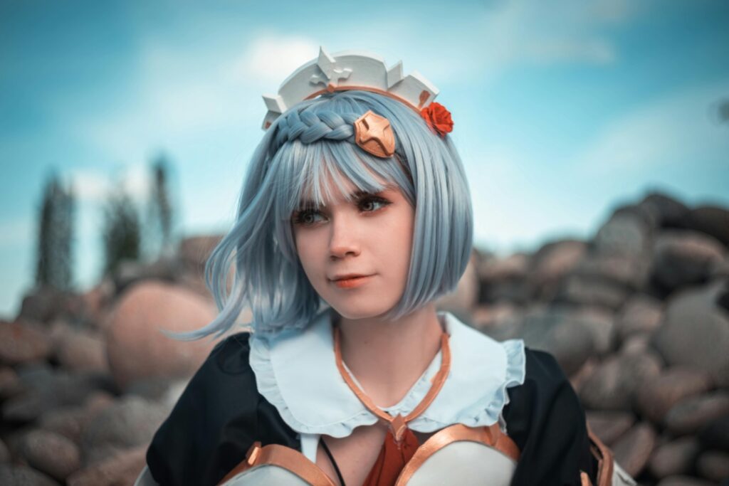 Person in cosplay with blue hair and a detailed outfit, posing outdoors in front of rocks and a blue sky.