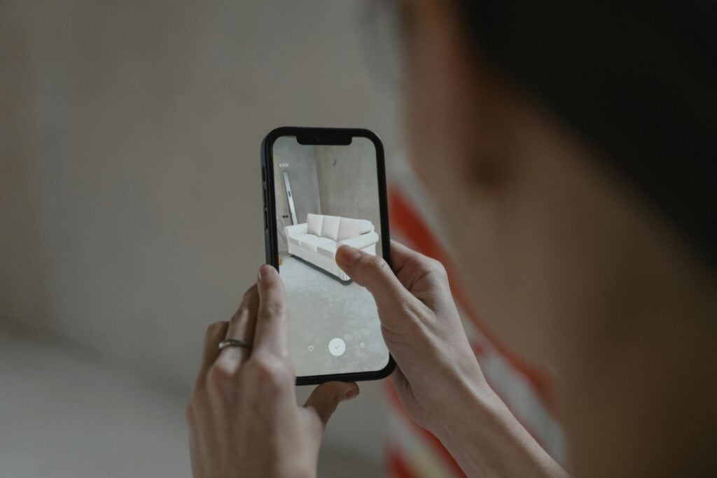 Person photographing a white sofa with a smartphone camera.