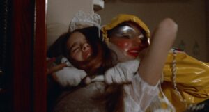A person in a clown costume grabs a struggling young girl wearing a white dress.