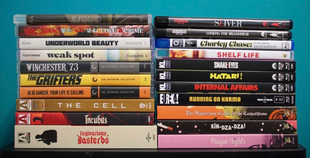 Stack of various DVD cases arranged against a teal background, featuring titles from multiple genres including "Inglourious Basterds" and "Winchester '73.