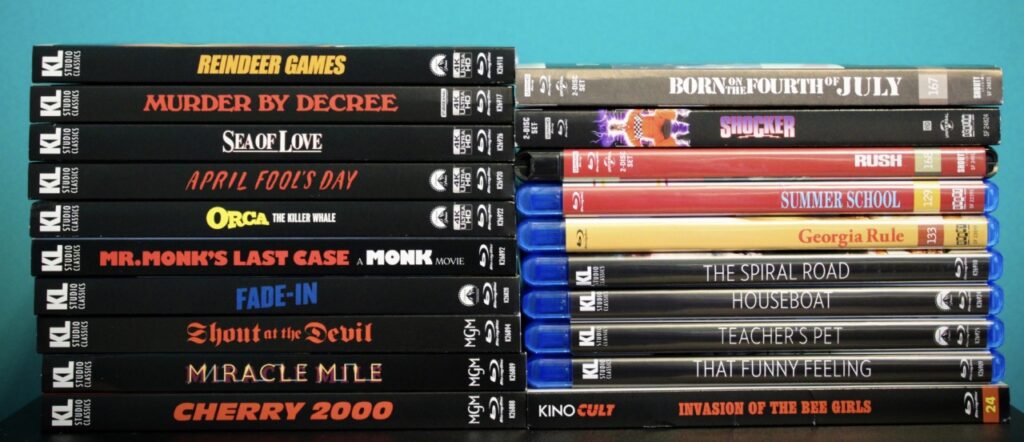 A stack of DVD and Blu-ray movies against a blue background, including titles like "Reindeer Games," "Born on the Fourth of July," and "Cherry 2000.