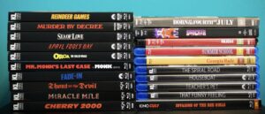A stack of DVD and Blu-ray movies against a blue background, including titles like "Reindeer Games," "Born on the Fourth of July," and "Cherry 2000.