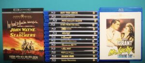 A stack of Blu-ray movies, featuring titles like "The Searchers" and "Mr. Lucky," displayed against a blue backdrop.