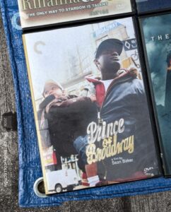 DVD cover of "Prince of Broadway" featuring a man holding a baby, with city elements in the background.