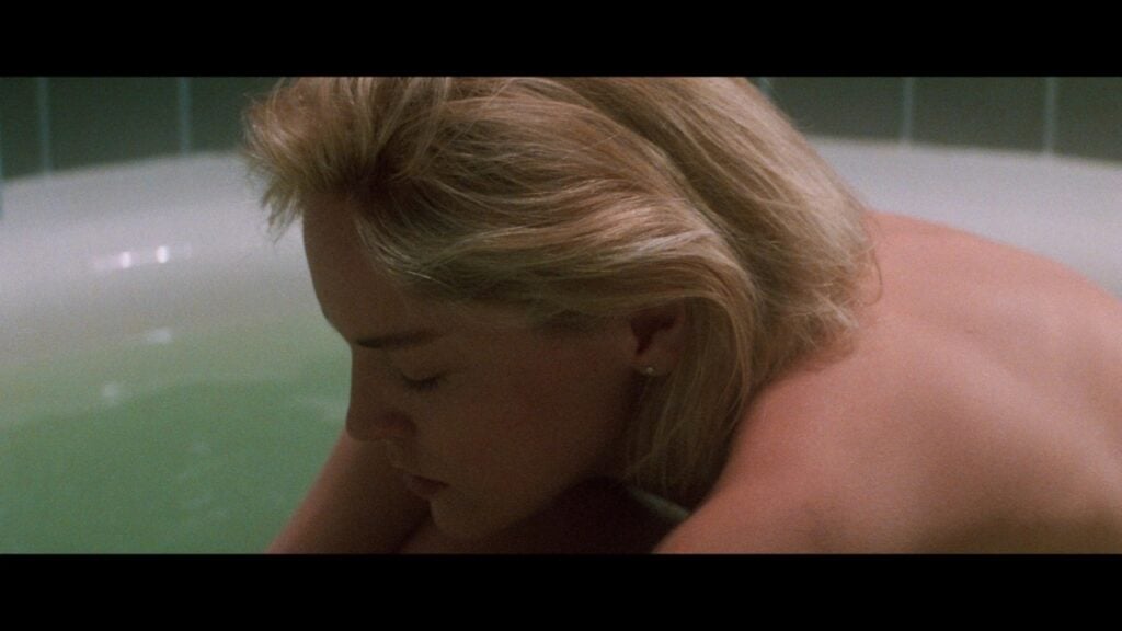 A person with short blonde hair sits in a bathtub with eyes closed, head resting on arms.