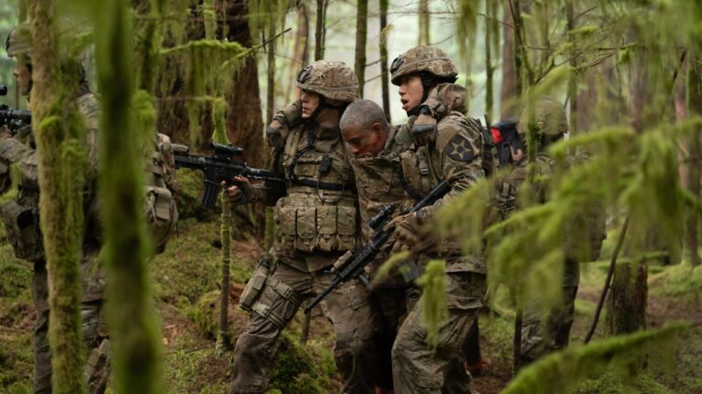 Soldiers in camouflage assist a man through a dense, mossy forest, with rifles and gear visible.