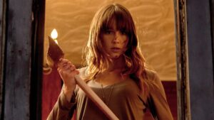 A person with long hair stands holding an axe, with marks on their face, looking determined.
