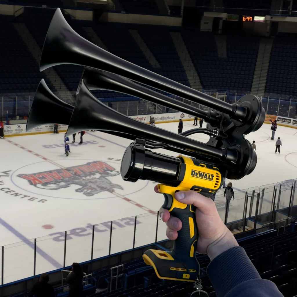 A person holding a Dewalt-branded handheld air horn device in an ice hockey arena with players on the rink.