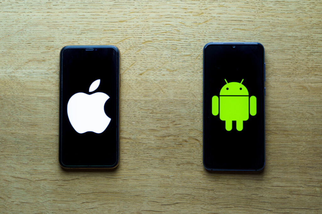 Two smartphones on a wooden surface; left shows Apple logo, right shows Android logo.