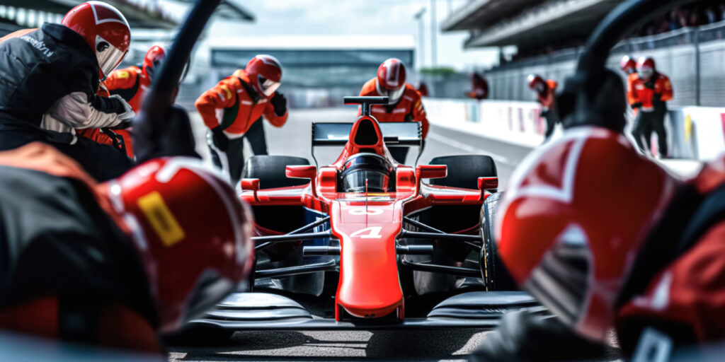 A red Formula 1 car in a pit stop, surrounded by a team of mechanics in red and black uniforms, with tire and tool handling.