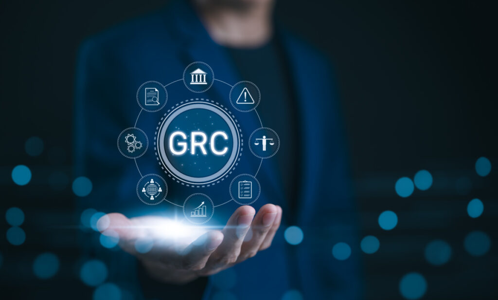 Person holding a digital GRC (Governance, Risk, Compliance) interface with various related icons floating around, symbolizing business management concepts.