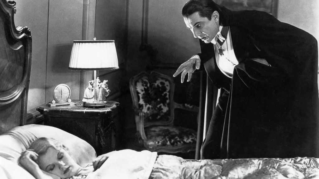 A man in a cape leans over a sleeping woman in a vintage bedroom while making a claw-like gesture with his hand.