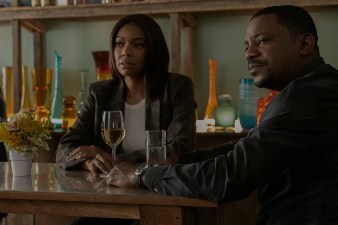Two people sit at a table with a glass of wine and a glass of water, surrounded by colorful vases on shelves in the background.