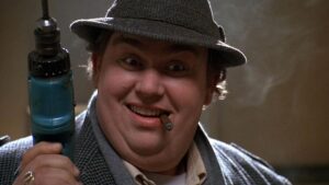 Person wearing a hat, smiling, and holding a power drill while a cigar is in their mouth.