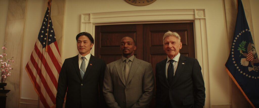 Three men in suits stand side by side in a formal room with an American flag and a presidential seal visible behind them.
