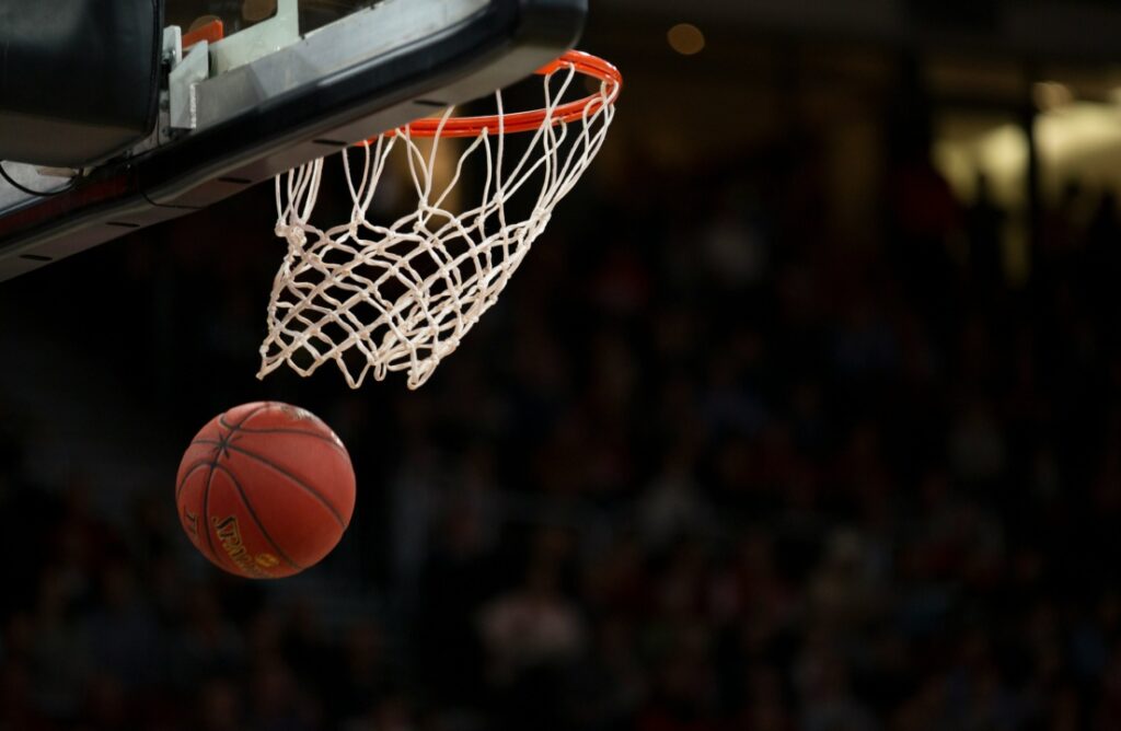A basketball is about to go through a hoop in an indoor stadium, with a blurred crowd in the background.