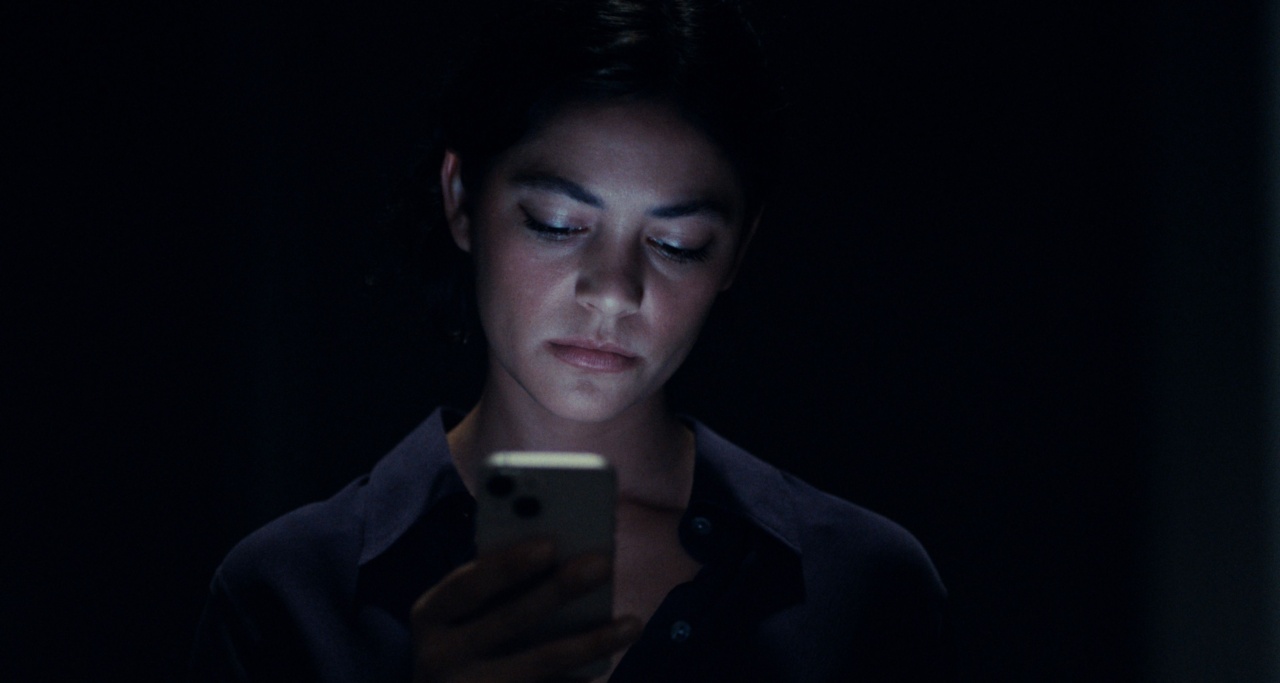 A person in a dark room looks down at a smartphone, which illuminates their face.