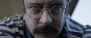 Epic Pictures’ DREAD Label Announces Release Date For True Crime Thriller ‘Ed Kemper’ A person wearing round glasses and a striped shirt looks directly into the camera with a neutral expression.