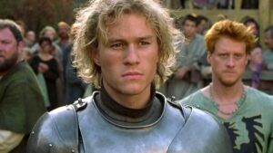Sony To Release Heath Ledger’s Action Favorite ‘A Knight’s Tale’ On 4K UHD Blu-Ray This May A person with curly hair and clad in medieval armor stands at the forefront, surrounded by a crowd.