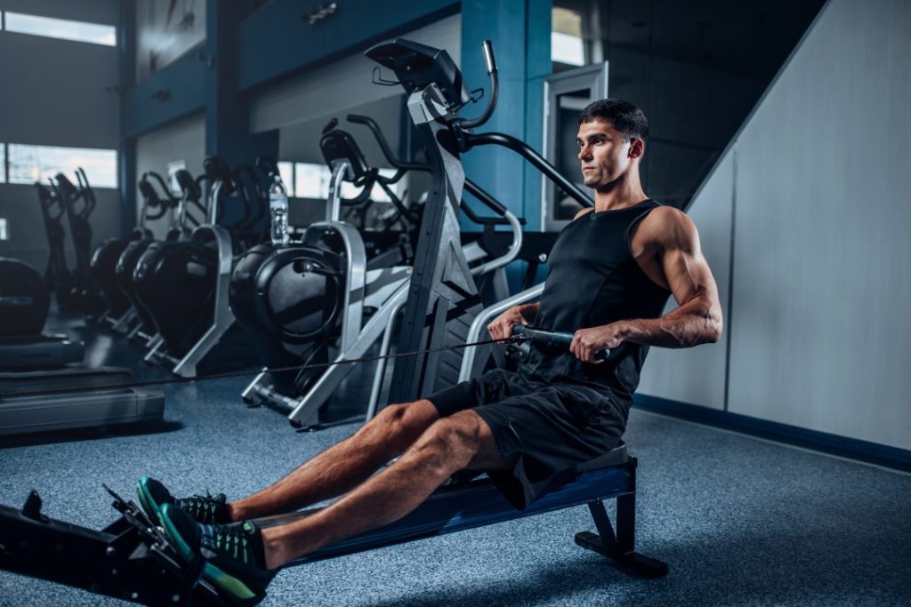 Person exercising on a rowing machine in a gym surrounded by various workout equipment.