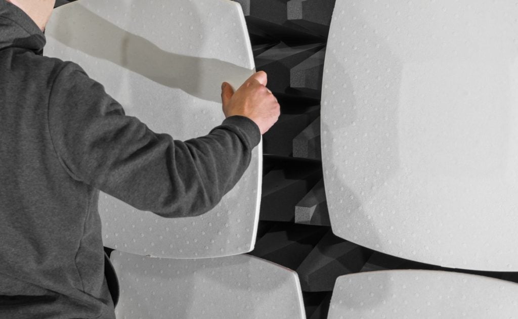 Person wearing a dark hoodie adjusts large, white, textured panels with black foam backing on a wall.