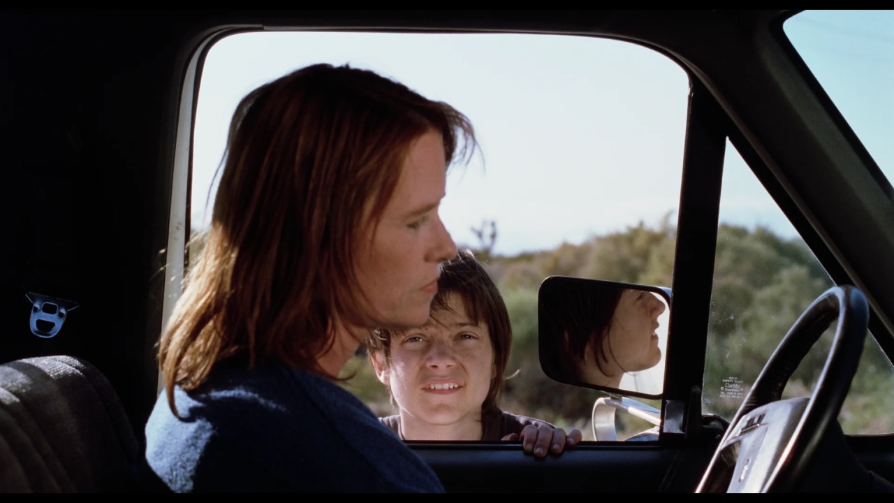 Woman sitting in a vehicle with the window open, while a boy stands outside looking in.
