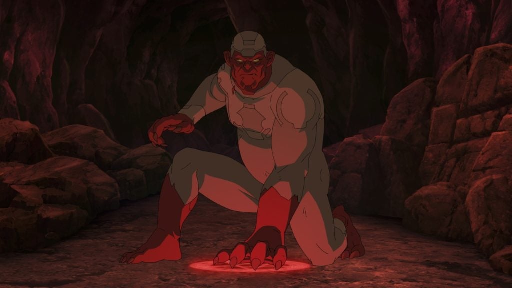 A creature with red skin and glowing eyes crouches inside a dark cave, wearing armor and resting one hand on a glowing red circle on the ground.