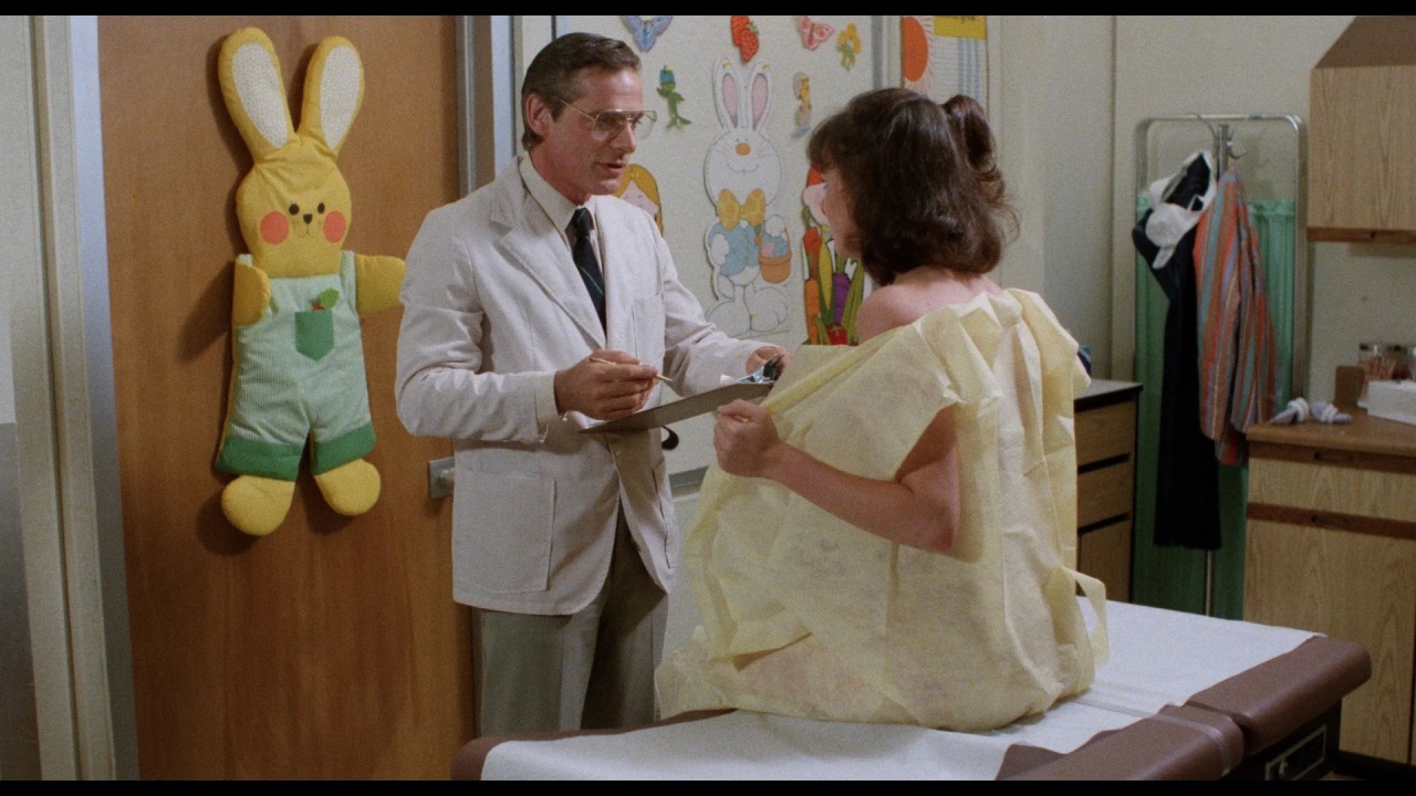 Doctor holding a clipboard talks to a patient sitting on an examination table in a medical office with child-friendly decor.