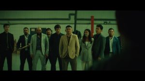 Group of people standing together indoors, with one person in a beige jacket in front.