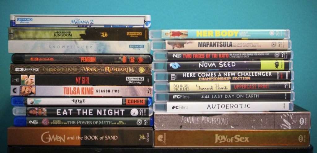 A collection of stacked DVD and Blu-ray movie cases against a blue background. Titles are visible on the spines.