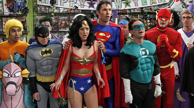 A group of people in superhero costumes stand in a comic book store, looking surprised.