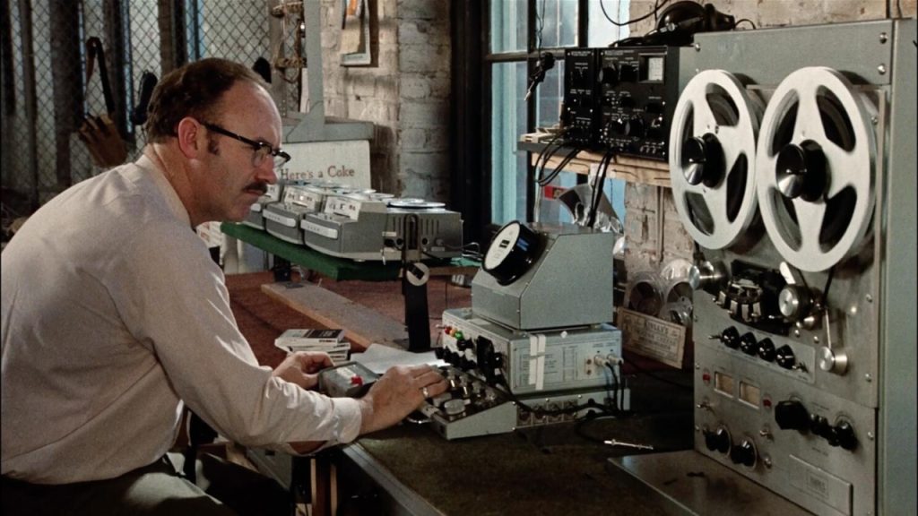 A man operates vintage audio and recording equipment in a workshop filled with electronic devices.