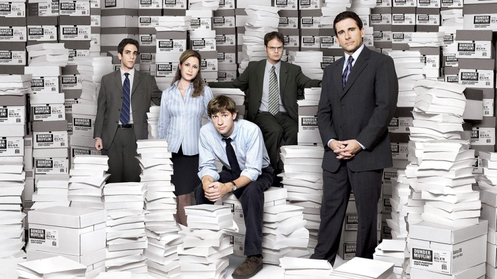 Five people in office attire pose amid stacks of paper and boxes, against a white background.