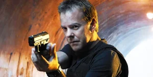 Person in dark clothing aiming a handgun intensely inside a tunnel with a light source behind them.