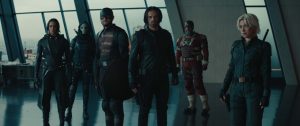 Six individuals in tactical outfits stand in formation inside a modern building with large windows. They carry various gear and weapons.