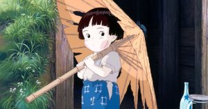 A young child stands outdoors holding a torn paper umbrella, wearing a white shirt and blue patterned shorts, with greenery and a wooden building in the background.