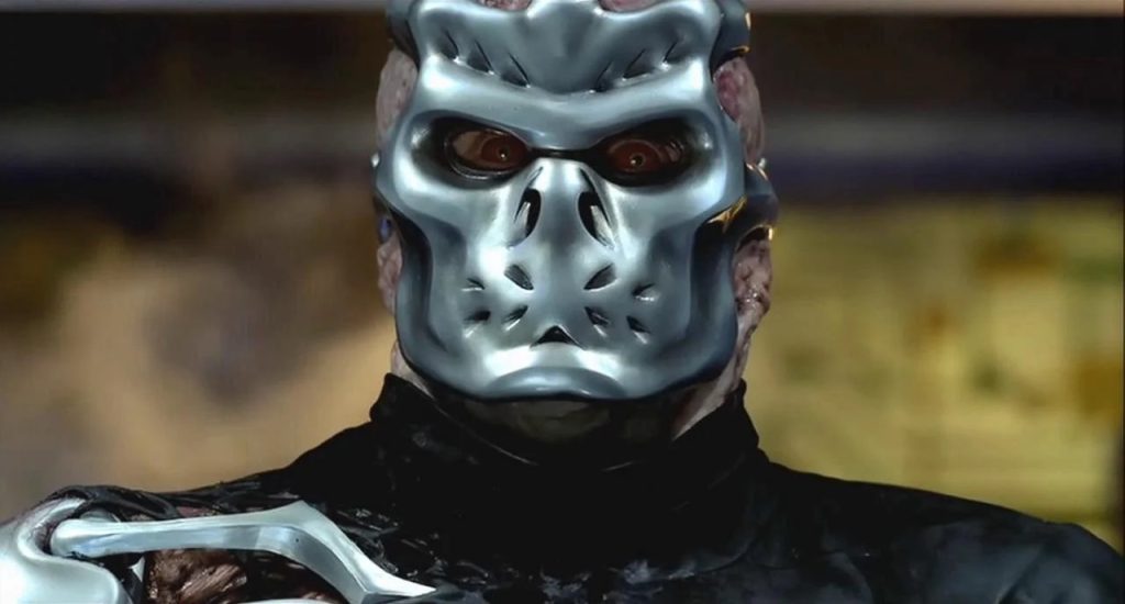 A person wearing a metallic, futuristic mask with animal-like features and dressed in dark clothing.