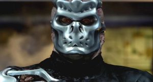 A person wearing a metallic, futuristic mask with animal-like features and dressed in dark clothing.