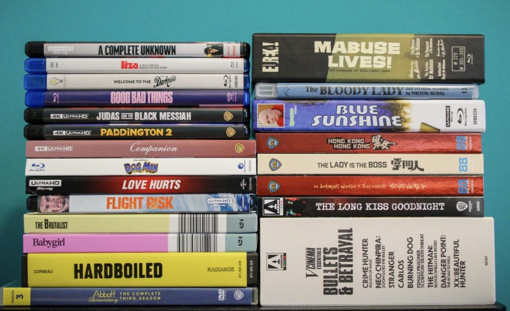 A collection of DVD and Blu-ray cases arranged in two stacks against a solid teal background. The titles vary across genres, including both films and series.