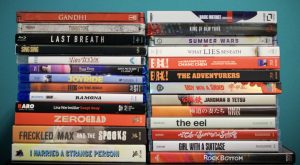 No Streaming Required: Physical Media Spotlight For The Week Of April 22nd A collection of DVD and Blu-ray movie cases stacked in three uneven columns against a light blue background. Titles include “Gandhi,” “Last Breath,” “King of New York,” and others.