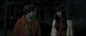 ‘Marshmallow’ Blu-Ray Review – Summer Camp Horror Film Offers Fun Twists & Turns A boy in an orange hoodie and a girl in a jacket stand in a dark, wooded area, looking at each other.